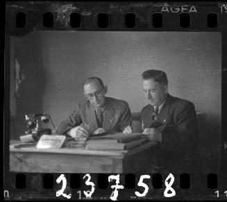 Transport Department administrator, Mr. Elefant (left), working at desk with member of the ghetto administration