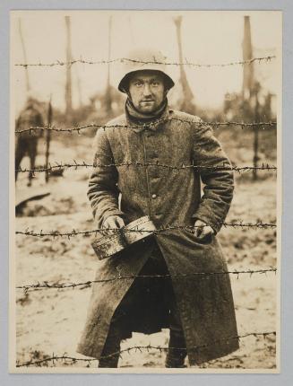 [Battle of Polygon Wood. A German prisoner holding a mess tin looks through the barbed wire of a POW camp at Langemarck, 26th September 1917]